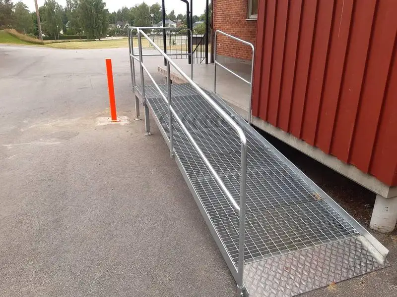 Galvaniserad handikappramp med räcken vid byggnad